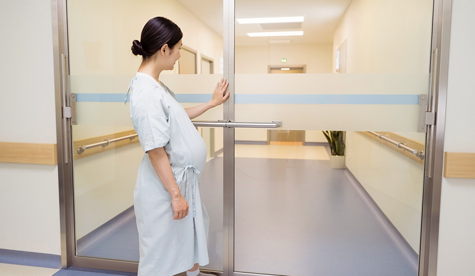 病院の扉を押す妊婦