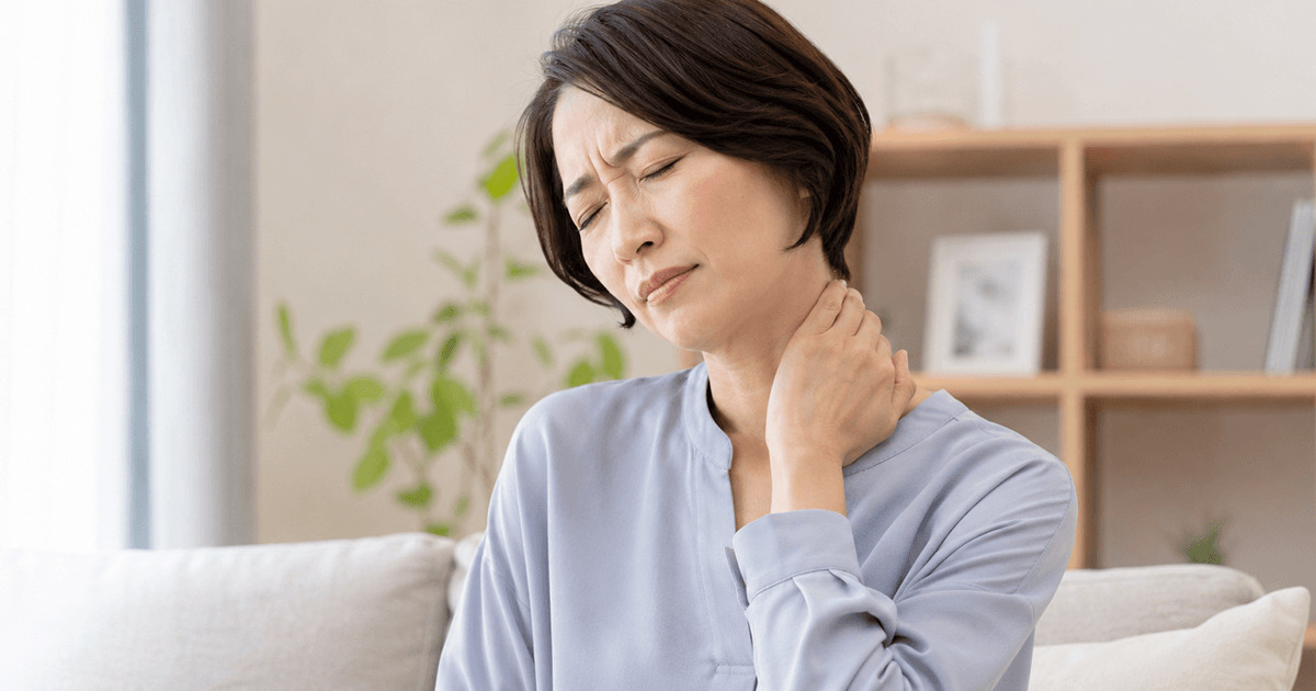 Woman on a sofa holds her neck with a pained expression, indicating neck discomfort at home.