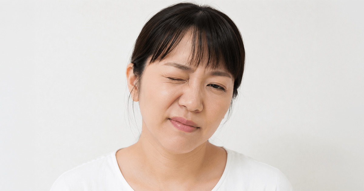 Portrait of a woman with dark hair in a white shirt, tilting her head and winking with a gentle smile against a light background.