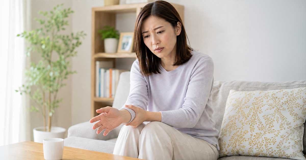 Woman sitting on a living-room sofa, examining her wrist with a concerned expression.